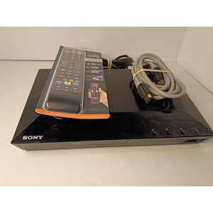 May include: A black Sony Blu-ray disc player with a remote control in its original packaging and a coiled grey HDMI cable. The remote packaging features text including Universal Remote and Sony branding on the player front panel.