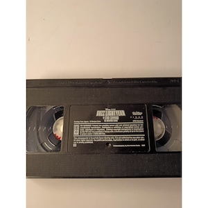 May include: A black VHS tape featuring the title Buzz Lightyear of Star Command The Adventure Begins. The label includes Disney and Pixar logos, FBI warning text, and technical specifications. The tape has two circular spools visible through windows.