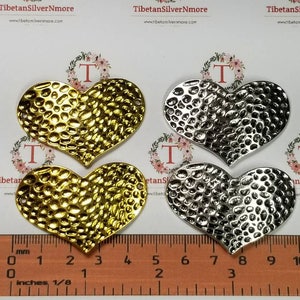 May include: Four metal heart-shaped charms, two gold and two silver, with a hammered texture. The charms are approximately 1.5 inches in size and are displayed on a ruler.