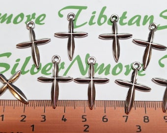 May include: A collection of silver-colored cross charms with a loop at the top for hanging. The crosses are displayed on a white surface with a ruler showing millimeters. The image also includes green text that reads "Nmore Tibetan Silver".