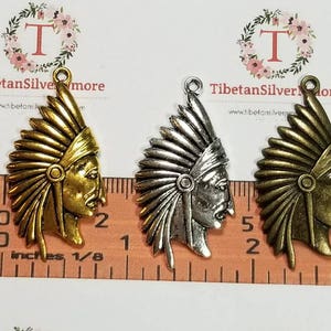 May include: Three metal Native American headdress charms in gold, silver, and bronze. The charms are about 2 inches tall and have a loop at the top for hanging.