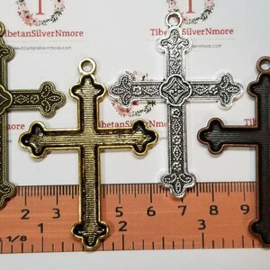 May include: Three metal cross charms in different finishes: antique gold, silver, and black. The crosses are ornate and detailed, with a decorative design. The charms are approximately 1 1/8 inches in size.