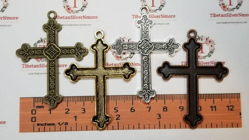 May include: Three metal cross charms in different finishes: antique gold, silver, and black. The crosses are ornate and detailed, with a decorative design. The charms are approximately 1 1/8 inches in size.