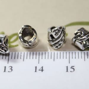 May include: Four silver metal beads with intricate designs. The beads are about 1.3 cm in diameter and have a hole in the center for threading.