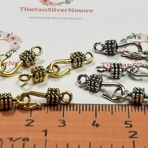 May include: Close-up of gold and silver toggle clasps with a hook and a beaded barrel. The clasps are shown on a ruler with inch markings.