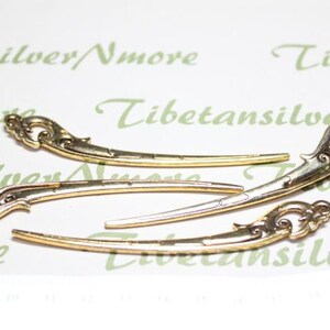May include: Three gold-colored metal hair clips with ornate designs. The clips are curved and have a decorative flourish at each end.