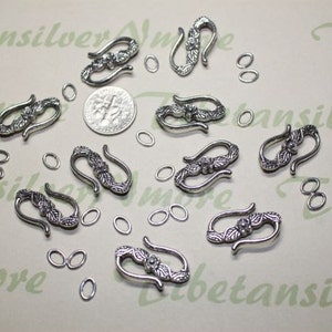 May include: Silver-toned metal clasps with floral designs. The clasps are about 2 inches long and have a hook shape. There are also several small silver-toned jump rings.