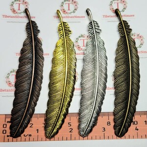 May include: Three metal feather charms in different finishes: antique copper, gold, and silver. Each charm is approximately 3 inches long and features a detailed feather design.