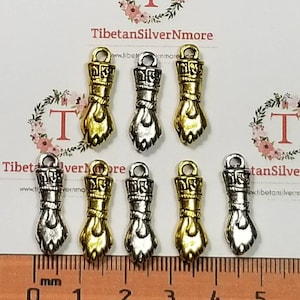 May include: Seven silver and gold charm pendants in the shape of a hand with a wrist band. The charms are approximately 1 inch long and are arranged in two rows on a white surface with a ruler in the bottom of the image.
