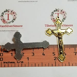 May include: Two gold-tone metal crucifixes, one with a figure of Jesus Christ, the other plain. The crucifixes are measured against a ruler with inches and millimeters.