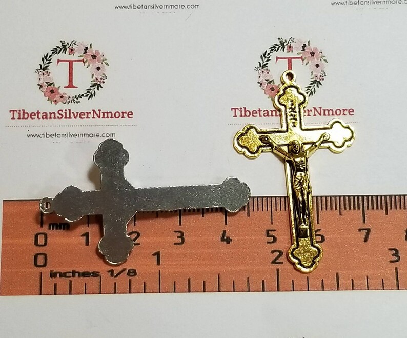 May include: Two gold-tone metal crucifixes, one with a figure of Jesus Christ, the other plain. The crucifixes are measured against a ruler with inches and millimeters.