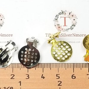 May include: Three earring clips, one silver, one gold, and one silver with a gold clip. Each clip has a round, perforated disc. The clips are measured on a ruler in inches.