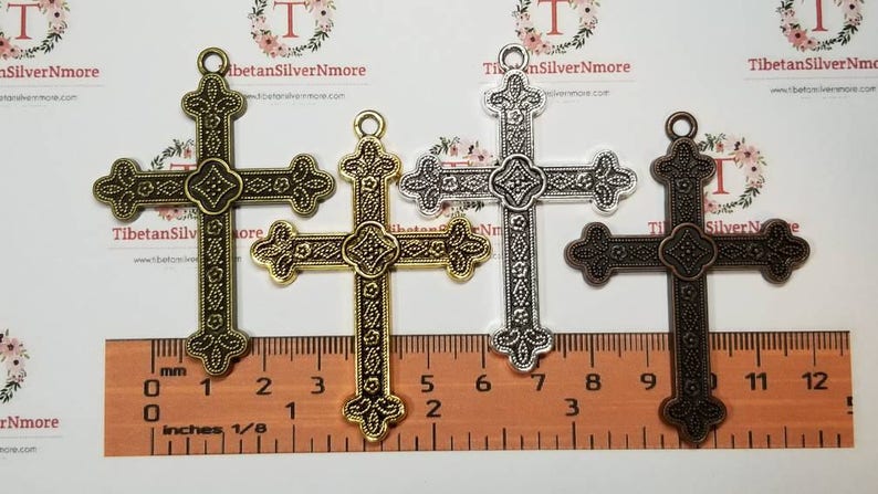 May include: Three ornate metal cross charms in gold, silver, and bronze finishes. Each cross measures approximately 2 inches in length. The crosses have a detailed design with intricate patterns and a slightly raised center.