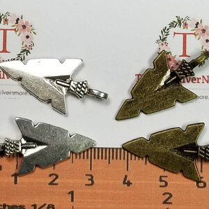 May include: Four arrowhead charms, two silver and two bronze, with a ruler for size reference. The charms are about 1 1/2 inches long.