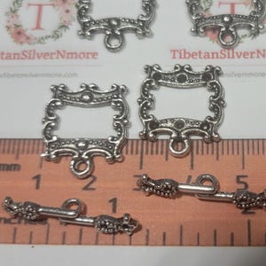 May include: Silver-toned metal frame with ornate details, measuring approximately 2 inches in length. The frame has a square opening and a small loop at the top.  The image also shows a silver-toned metal toggle clasp, measuring approximately 2 inches in length.  The clasp has a decorative design and two loops at each end.