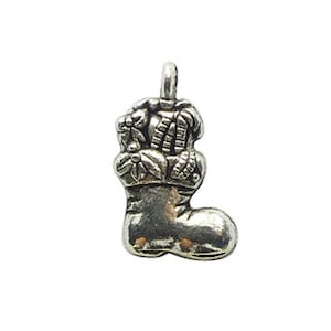 Może przedstawiać: Srebrny charm w kształcie choinkowej skarpetki wypełnionej ostrokrzewem i jagodami.