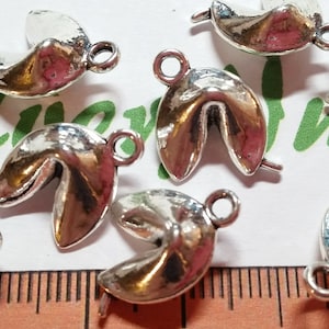 May include: Silver charm pendants shaped like fortune cookies with a hole for attaching to jewelry. The charms are about 1 inch in diameter.