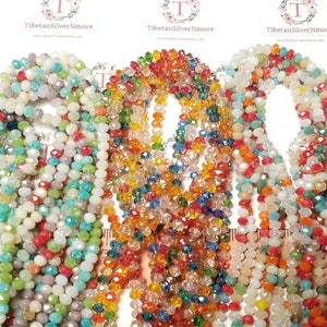 May include: Assortment of colourful faceted glass beads, with shades of blue, green, orange, red, and white. The beads are strung on a string and are arranged in a circular pattern.