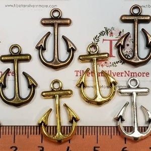 May include: Assortment of eight antique silver anchor charms in various sizes. The charms are in shades of silver, gold, and copper.