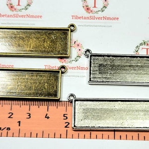 May include: Three rectangular metal frames with a brushed finish. The frames are different sizes and have two holes at the top for hanging. The frames are on a ruler with measurements in inches and millimeters.