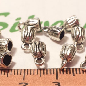 May include: Silver metal cord ends with a decorative design. The ends have a small loop for attaching to a cord or chain.