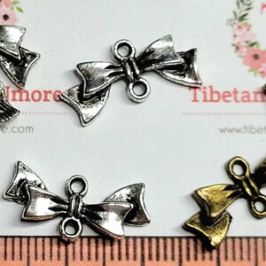 May include: A close-up of silver and gold bow charms with two loops. The charms are perfect for adding a touch of elegance to jewelry, crafts, and other projects.
