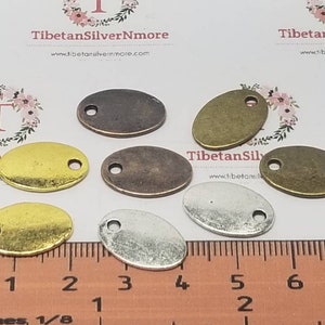 May include: Seven oval-shaped metal charms with a hole in the top. The charms are in various shades of gold, silver, and bronze. The charms are about 1 inch long and are arranged on a ruler with inch and millimeter markings.