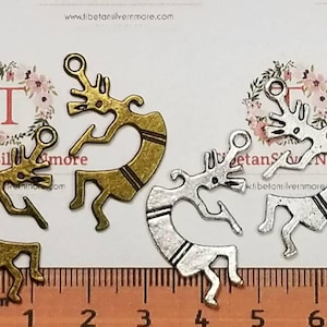 May include: Two metal charms in the shape of a stylized Native American dancer. One charm is gold and the other is silver. Both charms have a black stripe down the center. The charms are about 2 inches tall and are shown next to a ruler.