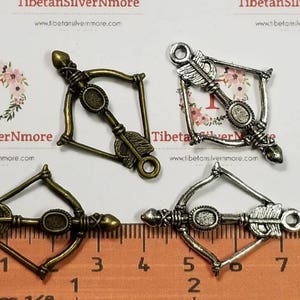 May include: Four antique silver and bronze bow and arrow charms. The charms are approximately 5 cm long and are perfect for jewellery making or scrapbooking.