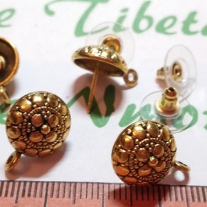 Puede incluir: Hallazgos de pendientes de tono dorado con un diseño redondo texturizado y un bucle en el lateral. Los hallazgos se muestran con un cierre de pendiente de plástico transparente.