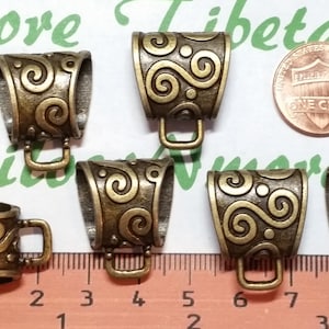 May include: Six antique gold-toned metal pendant caps with a swirl design. The caps are approximately 1 inch in length and have a loop at the top for attaching a pendant.