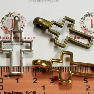 May include: Three metal cross charms in silver, gold, and bronze. The crosses are open and have a simple design. The charms are approximately 1 inch in size.