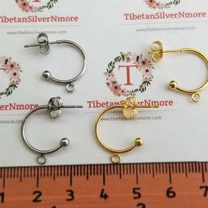 May include: A close-up shot of four half-hoop earrings. Two are silver-colored, and two are gold-colored. Each earring has a post for insertion, a small ball at the end of the hoop, and a small loop. The background has text that reads "TibetanSilverNmore".