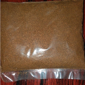 Puede incluir: Una bolsa de plástico transparente llena de un polvo fino de color marrón. El polvo parece tener un color y una textura uniformes, sin grumos ni variaciones visibles. La bolsa está sellada en la parte inferior.