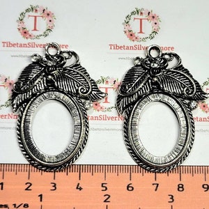 May include: Two silver-toned metal picture frame pendants with an oval opening. Each frame has a decorative design of leaves and a flower with a rhinestone in the center. The frames are approximately 2 inches in length.
