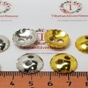 Könnte beinhalten: Acht Metall-Knopf-Abdeckungen, vier silberfarben und vier golden, mit jeweils zwei Löchern. Die Knopf-Abdeckungen haben einen gewellten Rand und sind auf einem Lineal mit Markierungen von 1 bis 10 angeordnet.