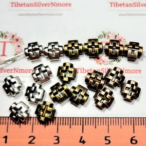 Puede incluir: Una colecci&oacute;n de cuentas de metal en forma de cruz, plateadas y bronce. Las cuentas miden aproximadamente 1 cm de tama&ntilde;o y tienen un dise&ntilde;o decorativo intrincado. Las cuentas est&aacute;n esparcidas sobre una regla con un fondo blanco.
