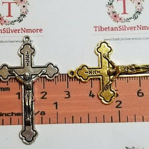 May include: Two silver and gold crucifixes with a figure of Jesus Christ on the cross. The crucifixes are measured against a ruler with inches and centimeters.