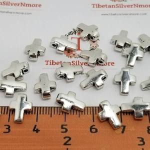 Puede incluir: Primer plano de una regla con abalorios de cruz de metal plateado. La regla está marcada en pulgadas y los abalorios están esparcidos sobre la regla.