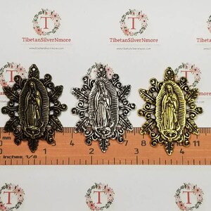 Puede incluir: Tres encantos de metal con una figura religiosa en un marco decorativo. Los encantos son de color dorado, plateado y bronce. Los encantos miden aproximadamente 5 cm de largo.