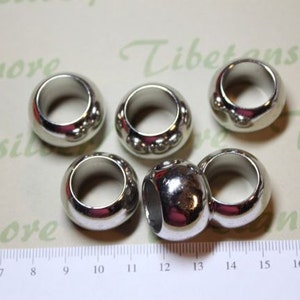 May include: Six silver metal rings with a smooth, rounded surface. The rings have a small, raised design around the edge.