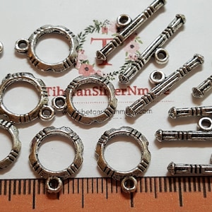 May include: A collection of silver-toned metal toggle clasps and jump rings. The toggle clasps have a decorative design and are approximately 1 inch long. The jump rings are round and have a diameter of about 1/2 inch.