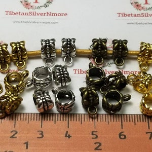 May include: Assortment of 18 silver, gold, and bronze metal bead caps with decorative designs. The bead caps have a loop at the top and are approximately 1 inch in length.
