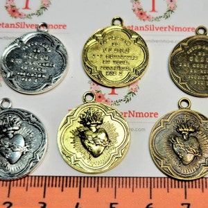 Op de afbeelding: Zes zilveren en gouden metalen hangers met religieuze afbeeldingen. De hangers tonen een hart met een doornenkroon en vlammen, en de woorden "Jesus" en "J'ai confiance en vous" in het Frans.
