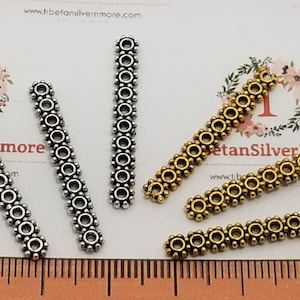May include: Four silver and four gold metal spacer beads with a decorative design. The beads are arranged in two rows on a white surface. The beads are approximately 2.5 cm long.