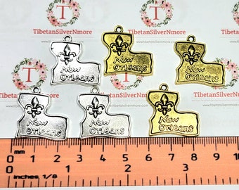 May include: Five silver and gold charms shaped like the state of Louisiana with the words "New Orleans" and a fleur-de-lis design. The charms are approximately 2.5 cm in size and are displayed on a ruler.