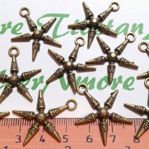 May include: Eight antique gold-toned metal charms shaped like six-pointed stars with pointed tips. Each charm has a loop at the top for attaching to a necklace, bracelet, or other jewelry.