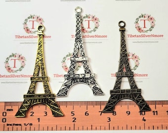 Peut inclure: Trois breloques en métal en forme de tour Eiffel, en or, argent et noir. Les breloques mesurent environ 10 cm de haut et sont présentées à côté d'une règle.
