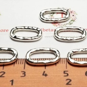 May include: Six silver oval jump rings with a hammered texture. The rings are approximately 1 inch in length and 1/2 inch in width. They are measured against a ruler.
