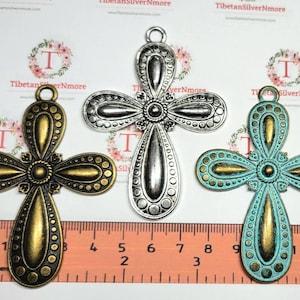 May include: Three ornate metal cross charms in different colors: gold, silver, and turquoise. Each cross has a detailed design with raised dots and a center circle. The crosses are approximately 2 inches in length.